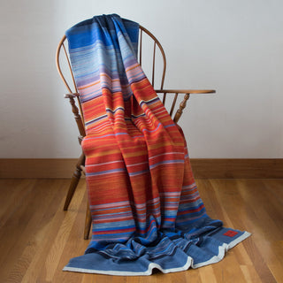 A Swans Island handwoven Horizon throw draped on a chair.  This throw features richly hand-dyed wool yarns in vibrant shades of orange and blue.