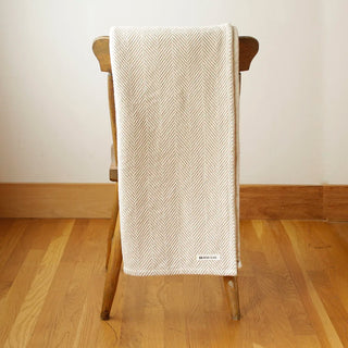 Suggestion


A cream and beige colored woven throw blanket with a herringbone pattern draped over the back of a wooden chair in a minimalist room with light wood floors and a beige wall.

