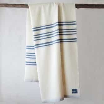 A Swans Island Grace blanket with blue stripes draped on a branch.