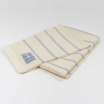 Casa Branca x Swans Island - Branca Ticking Stripe Throw . 100% soft merino wool with hand-dyed stripes and ivory silk binding. Handwoven in Maine. Shown here in Sky.