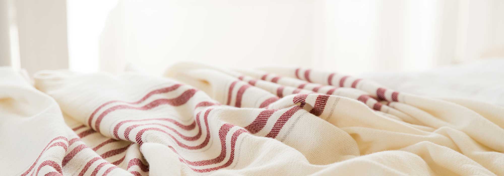 rumpled white blanket with red stripes on bed