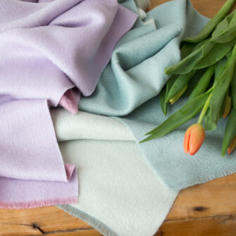 Swans Island Company's Reversible Suri Alpaca Scarf in Aquamarine / Soft Aqua and Soft Pink / Light Purple,shown with coral tulips.