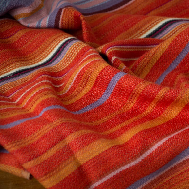 Swans Island Company's Horizon Limited Edition 2026 Throw - A tangible homage to the vibrant colors of first light and golden hour when the sun rises and sets. Handwoven in Maine with hand-dyed wools - a textiles collectors piece. A closeup detail of the shades of sun orange reflecting on the water.