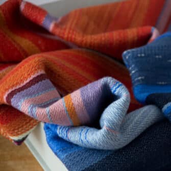 Swans Island Company's Horizon Limited Edition 2026 Throw - A tangible homage to the vibrant colors of first light and golden hour when the sun rises and sets. Handwoven in Maine with hand-dyed wools - a textiles collectors piece. A closeup detail of the transition from water to sky.