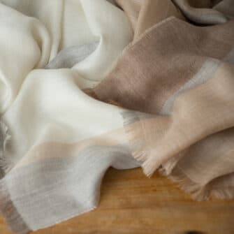 Swans Island Company's Gossamer Alpaca Wrap is whisper thin baby alpaca in undyed natural colors. Ivory with light beige and light grey closeup detail showing fringed edges.